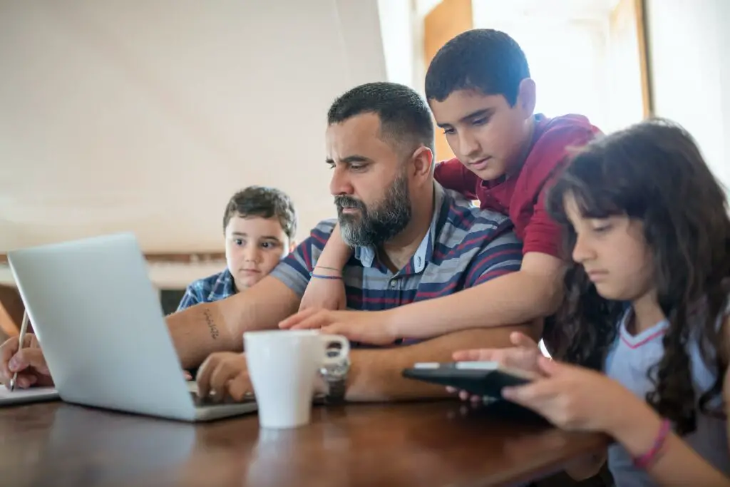 A father with children at a table with laptop, note pad and calculator - symbolizing the joint budgeting process of the family