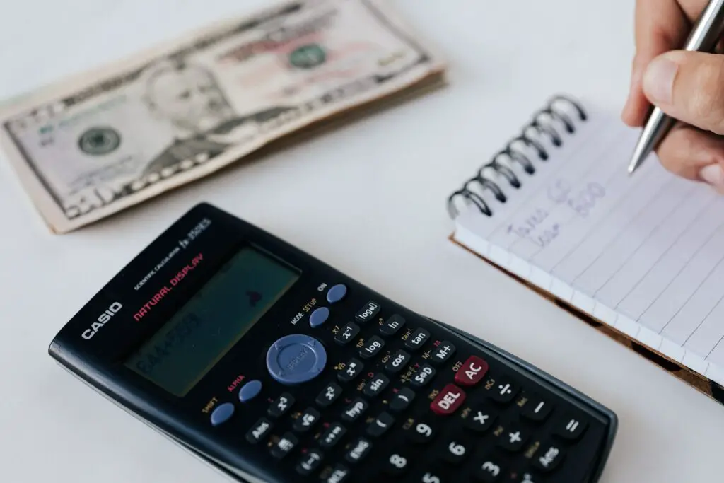 A calculator, some money and someone writing expenses on a notepad - symbolizing the budgeting process