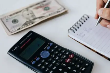 A calculator, some money and someone writing expenses on a notepad - symbolizing the budgeting process